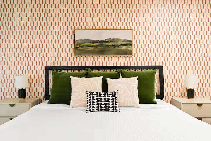 Bedroom with green velvet pillows and orange striped wallpaper