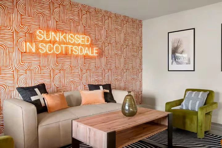 Sitting room with neon sign, tan sofa and green armchair